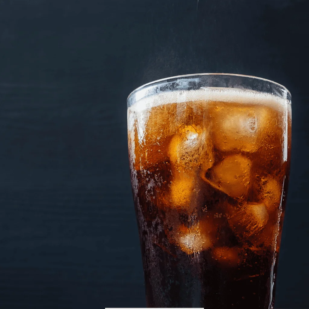 A glass of chilled homemade Olipop-inspired soda fizzing on top and served with ice in it on a black background